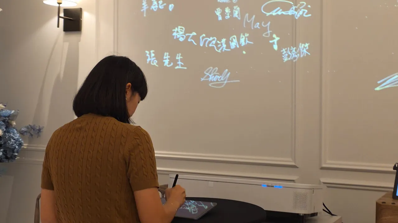 賓客的背影，正在桌前簽名，上方的牆上是其他人的簽名